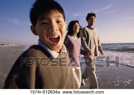 Stock Image - Parents and their son walking on the beach. Fotosearch