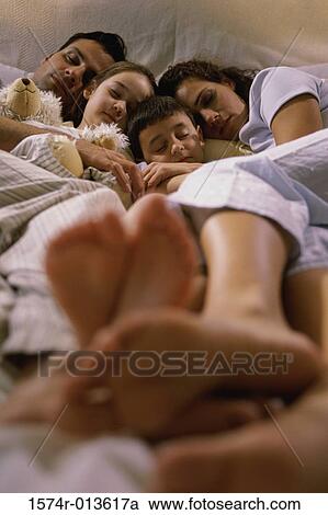 Stock Image - Parents and their two children sleeping together in bed. Fotosearch