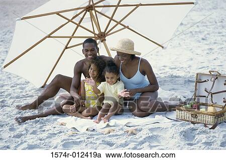 Parents and their two daughters sitting under a beach umbrella on the beach View Large Photo Image Stock Image - Parents and their two daughters sitting under a beach umbrella on the beach. Fotosearch