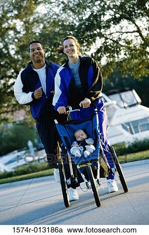 Stock Image - Parents jogging with their daughter in a baby stroller. Fotosearch