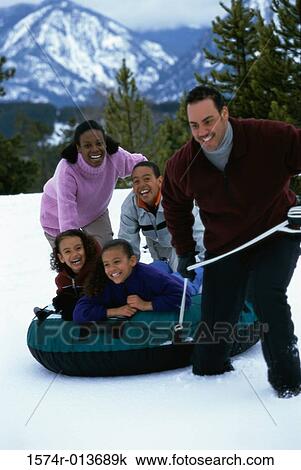 Stock Image - Parents playing with their three children in snow. Fotosearch