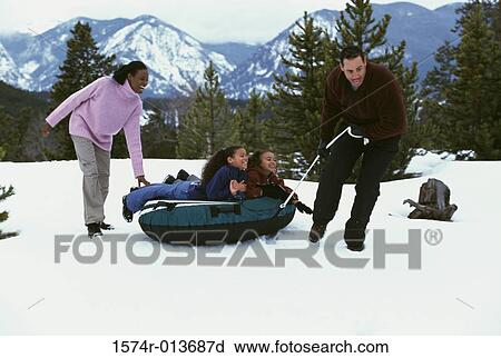 Stock Image - Parents pulling an inflatable tube with their two daughters. Fotosearch