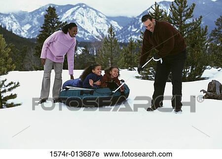 Stock Image - Parents pulling an inflatable tube with their two daughters. Fotosearch