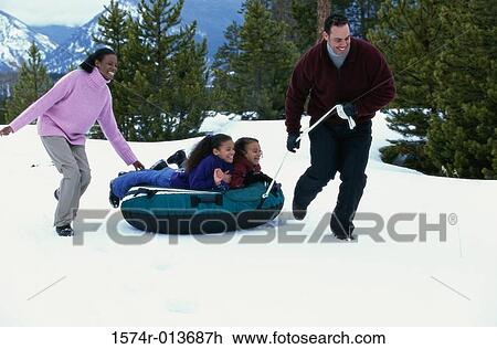 Stock Image - Parents pulling an inflatable tube with their two daughters. Fotosearch