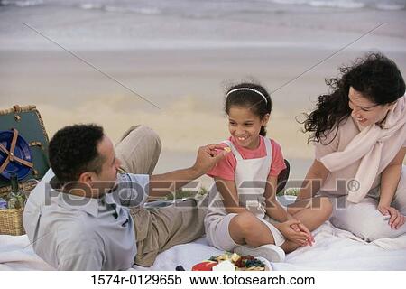 Stock Image - Parents sitting with their daughter on the beach. Fotosearch