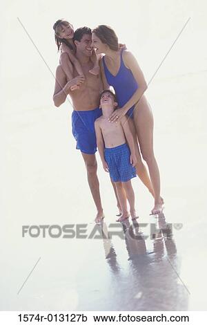 Stock Image - Parents standing with their two children on the beach. Fotosearch