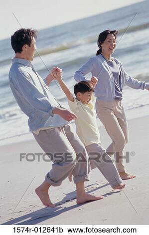 Stock Image - Parents walking with their son on the beach. Fotosearch
