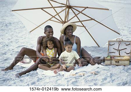 Stock Image - Parents with their two daughters sitting on the beach. Fotosearch