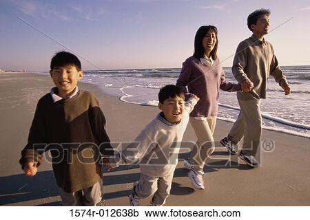 Stock Image - Parents with their two sons walking on the beach. Fotosearch