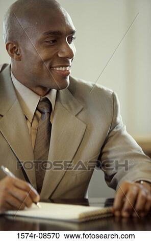 Portrait of a businessman seated at an office desk writing in a notepad View Large Photo Image Stock Image - Portrait of a businessman seated at an office desk writing in a notepad. Fotosearch
