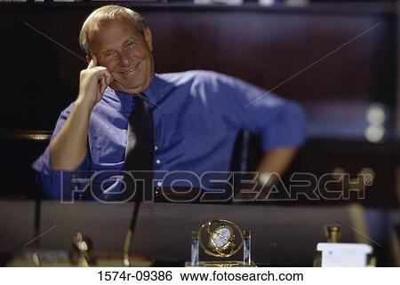 Portrait of a businessman seated behind an office desk smiling View Large Photo Image Stock Photograph - Portrait of a businessman seated behind an office desk smiling. Fotosearch