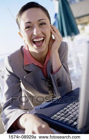 Stock Image - Portrait of a businesswoman laughing while sitting in front of a laptop. Fotosearch