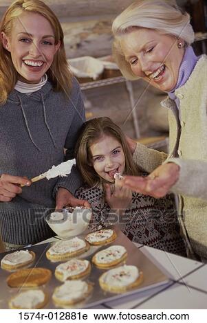 Stock Image - Portrait of a daughter tasting cookies being prepared by her mother and grandmother. Fotosearch