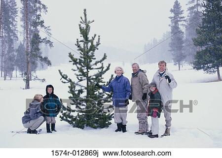 Stock Image - Portrait of a family standing in front of a Christmas tree in snow. Fotosearch