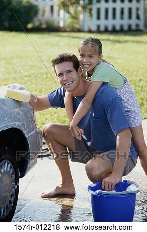 Stock Photo - Portrait of a father washing a car with his daughter hugging him from behind. Fotosearch