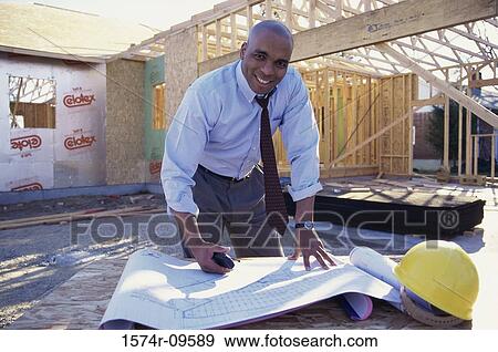 Portrait of a male architect working on blueprints at a construction site View Large Photo Image Stock Photo - Portrait of a male architect working on blueprints at a construction site. Fotosearch