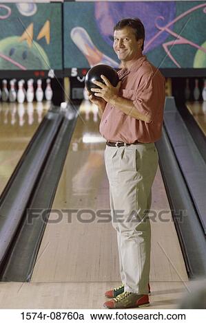 Stock Image - Portrait of a man holding a bowling ball in a bowling alley. Fotosearch