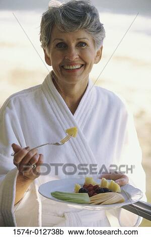 Stock Image - Portrait of a mature woman eating fruit salad. Fotosearch