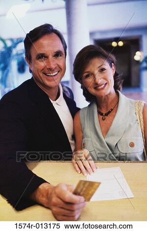 Portrait of a mid adult couple holding a credit card at a hotel reception desk View Large Photo Image Stock Photography - Portrait of a mid adult couple holding a credit card at a hotel reception desk. Fotosearch