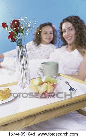 Stock Image - Portrait of a mother and daughter in bed together with a breakfast tray. Fotosearch