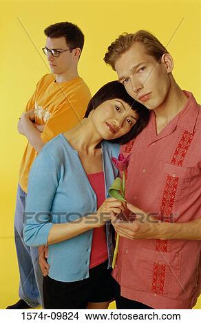 Picture - Portrait of a young couple holding each other with a young man standing behind them. Fotosearch