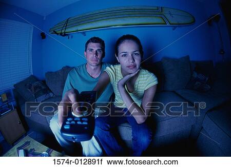 Stock Image - Portrait of a young couple sitting on a couch watching television. Fotosearch