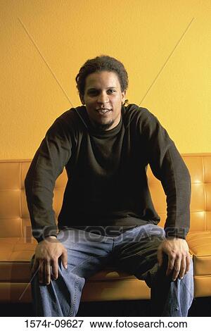 Stock Photo - Portrait of a young man sitting on a couch. Fotosearch