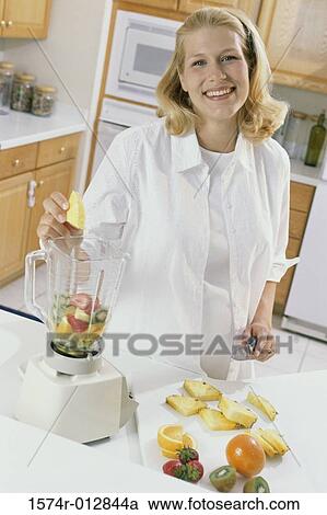 Stock Image - Portrait of a young pregnant woman putting fruit in a blender. Fotosearch