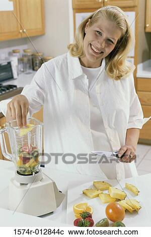 Stock Image - Portrait of a young pregnant woman putting slices of fruits in a food processor. Fotosearch