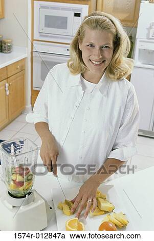 Stock Image - Portrait of a young pregnant woman cutting fruit. Fotosearch