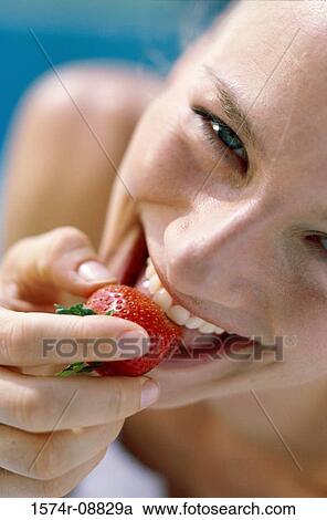 Stock Image - Portrait of a young woman eating a strawberry. Fotosearch