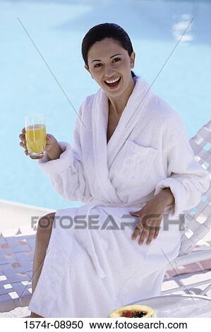 Stock Image - Portrait of a young woman sitting poolside with a glass of orange juice. Fotosearch