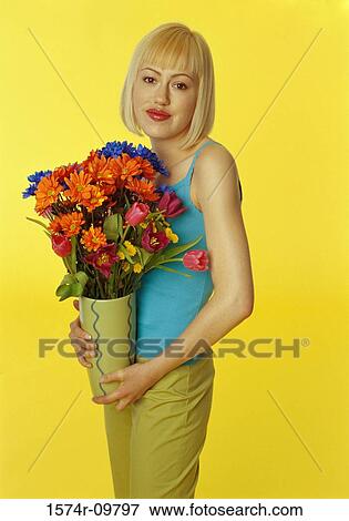 Stock Photo - Portrait of a young woman standing holding a vase of flowers. Fotosearch