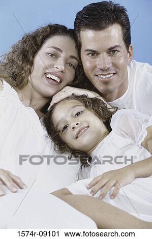 Stock Image - Portrait of parents and their daughter lying in bed together. Fotosearch