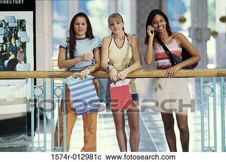 Stock Image - Portrait of three teenage girls standing with shopping bags. Fotosearch
