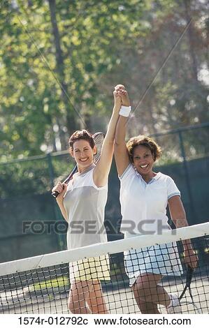 Stock Image - Portrait of two mid adult women cheering after winning a tennis match. Fotosearch