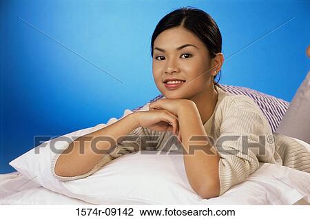 Stock Image - Portrait of young woman lying on a bed smiling. Fotosearch