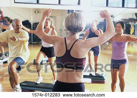 Stock Image - Rear view of a female aerobics instructor giving instruction in a step aerobics class. Fotosearch