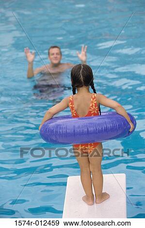 Stock Photo - Rear view of a girl standing with an inflatable ring on the diving board. Fotosearch