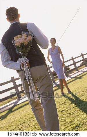 Stock Image - Rear view of a mature man holding a bouquet of flowers behind his back. Fotosearch