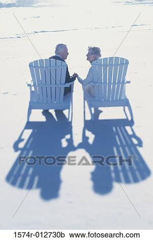 Stock Image - Rear view of a senior couple sitting together on the beach. Fotosearch