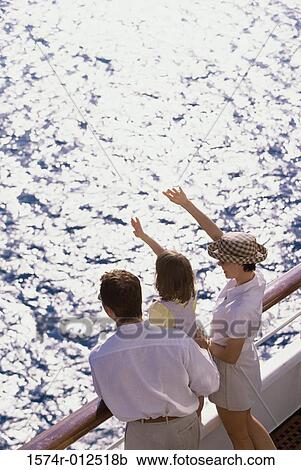 Stock Image - Rear view of a young couple and their daughter standing on a cruise ship waving. Fotosearch
