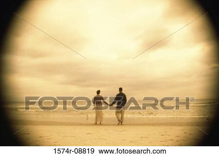 Rear view of a young couple holding hands on the beach View Large Photo Image Stock Photo - Rear view of a young couple holding hands on the beach. Fotosearch