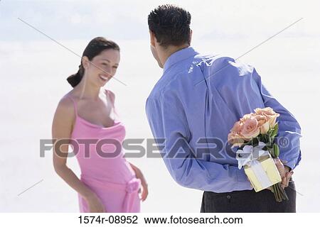 Rear view of a young man hiding a bouquet of flowers from a young woman View Large Photo Image Stock Image - Rear view of a young man hiding a bouquet of flowers from a young woman. Fotosearch
