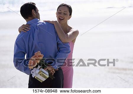 Rear view of a young man hiding a bouquet of flowers from a young woman View Large Photo Image Stock Photo - Rear view of a young man hiding a bouquet of flowers from a young woman. Fotosearch