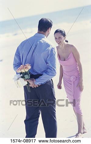 Rear view of a young man holding a gift and flowers behind his back View Large Photo Image Stock Photo - Rear view of a young man holding a gift and flowers behind his back. Fotosearch