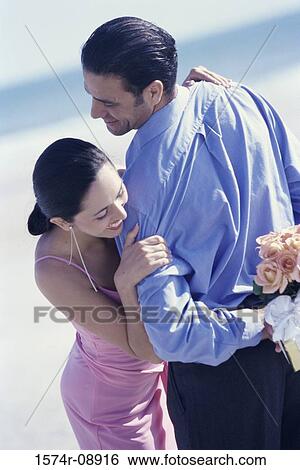 Rear view of a young man holding a gift and flowers behind his back View Large Photo Image Stock Photograph - Rear view of a young man holding a gift and flowers behind his back. Fotosearch