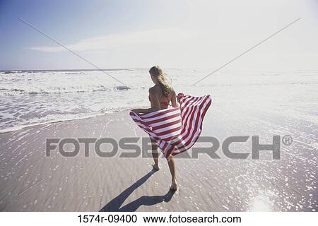 Rear view of a young woman standing on the beach holding a towel View Large Photo Image Stock Image - Rear view of a young woman standing on the beach holding a towel. Fotosearch