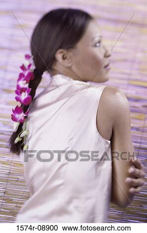 Stock Image - Rear view of a young woman wearing orchid flowers in her hair. Fotosearch