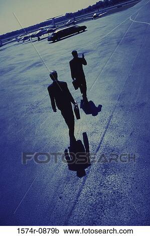 Stock Image - Rear view of two businessmen walking in an airport. Fotosearch